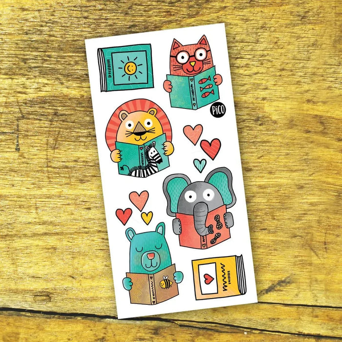 A sheet of colorful cartoon animal tattoos featuring a lion, cat, elephant, and bear reading books, displayed on a rustic wooden surface.