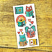 A sheet of colorful cartoon animal tattoos featuring a lion, cat, elephant, and bear reading books, displayed on a rustic wooden surface.