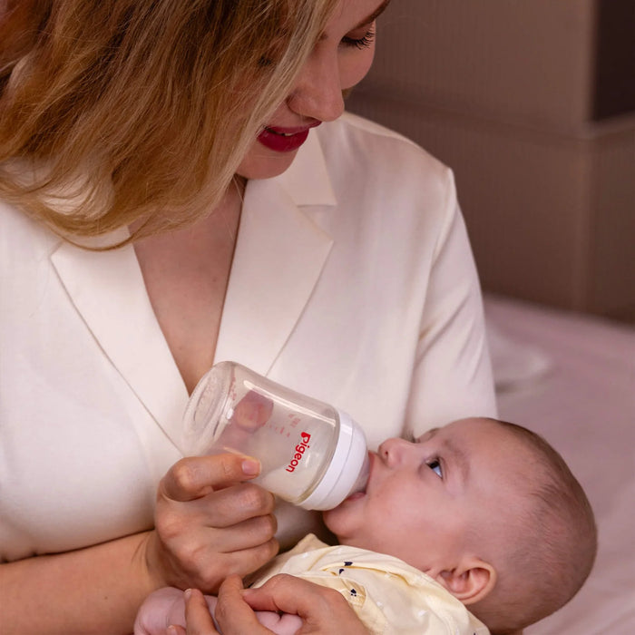Woman feeding a baby with a Pigeon brand bottle, both wearing white outfits.