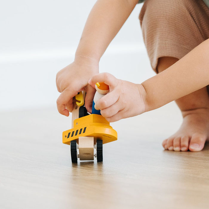 Child's hands playing with a yellow toy construction truck on a light wooden floor.