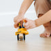 Child's hands playing with a yellow toy construction truck on a light wooden floor.