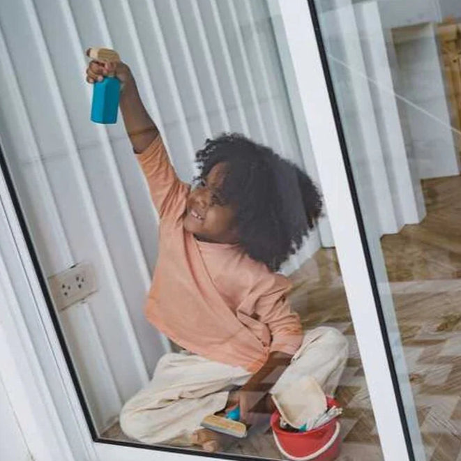 child cleaning a glass door with a make believe toy spray bottle in a home setting.