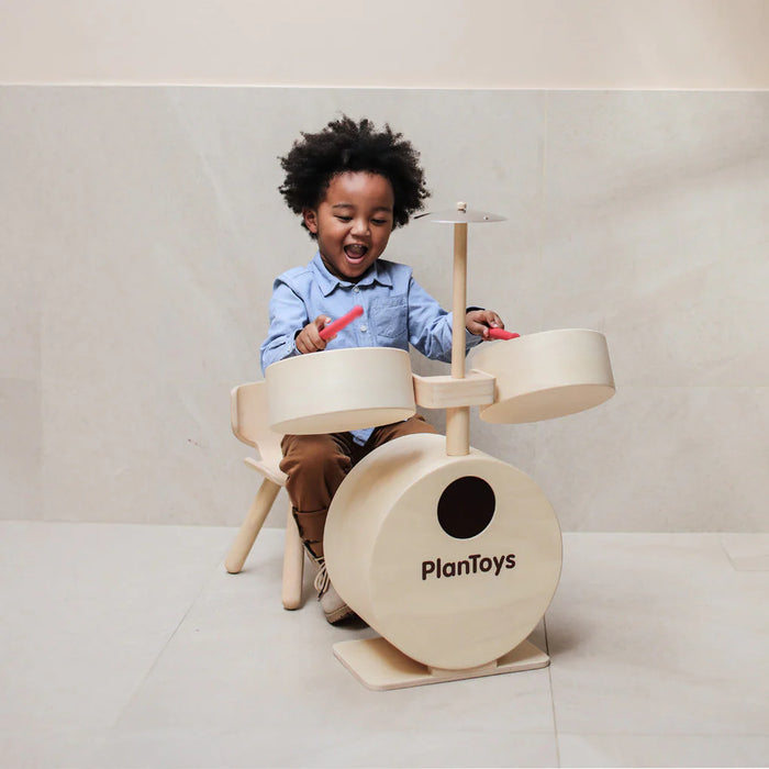 Child playing with a toy drum set on a light gray background