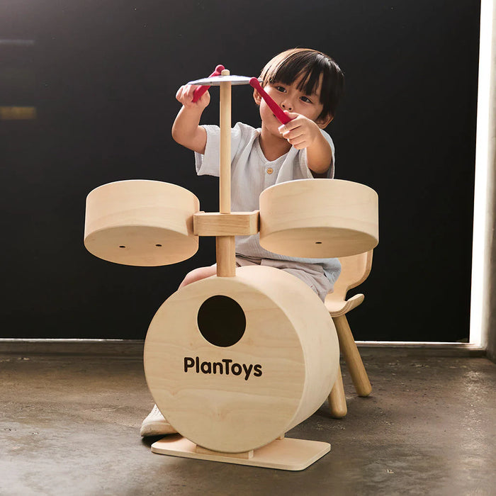 Child playing with a wooden drum set labeled 'PlanToys' against a dark background