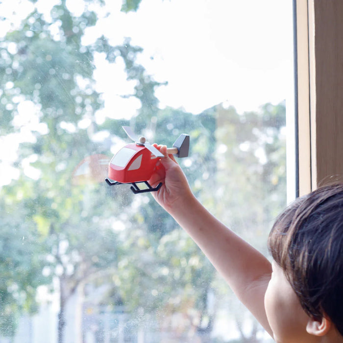 A child plays with a red toy helicopter shown in front of a window