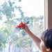 A child plays with a red toy helicopter shown in front of a window