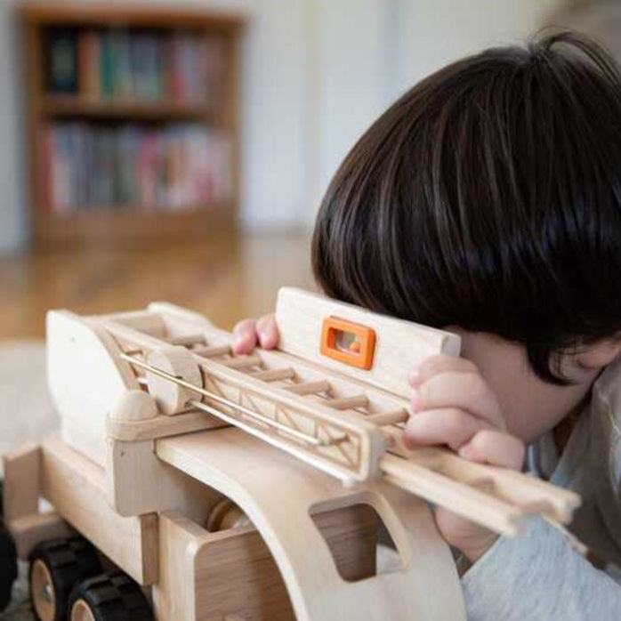 Child playing with a wooden toy truck and a level in a room with bookshelves.