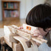 Child playing with a wooden toy truck and a level in a room with bookshelves.