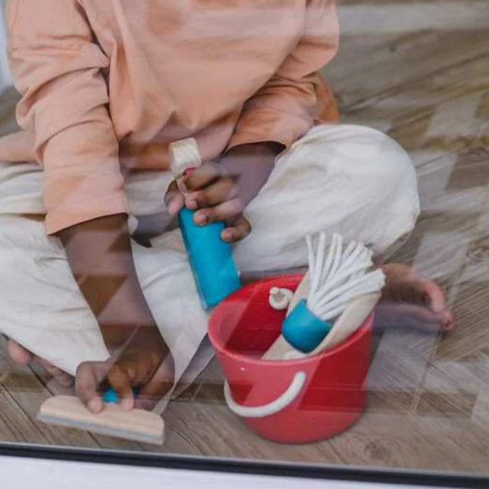 Child playing with toy cleaning set on a wooden floor