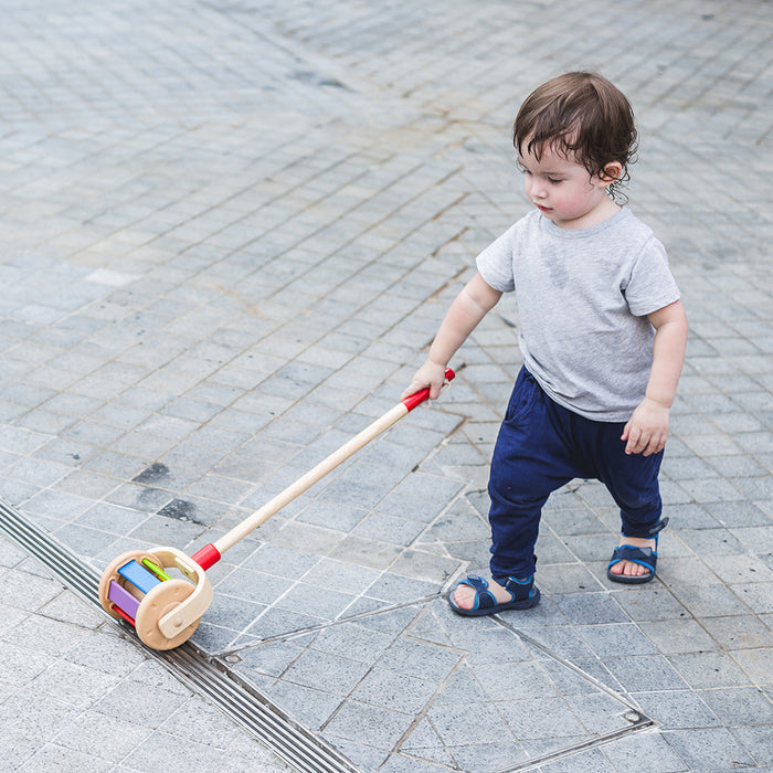 Child pushing a wooden toy with colorful wheels on a paved walkway