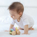 Baby playing with colorful wooden car toy on a white surface