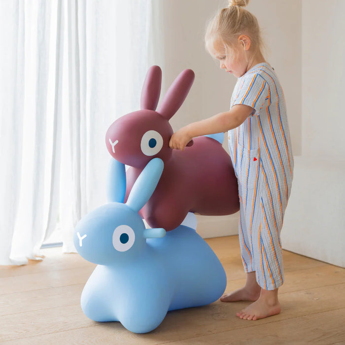 Child playing with a blue and pink rabbit-shaped toy on a wooden floor.