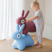 Child playing with a blue and pink rabbit-shaped toy on a wooden floor.