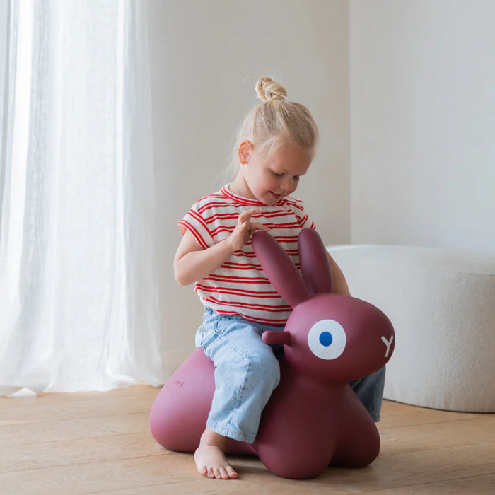 Child sitting on a pink bunny-shaped cushion in a bright room.