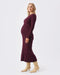 Side profile of pregnant woman wearing a long sleeved maroon maternity dress against a white background