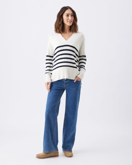 pregnant woman with striped sweater and maternity jeans stands against a white background