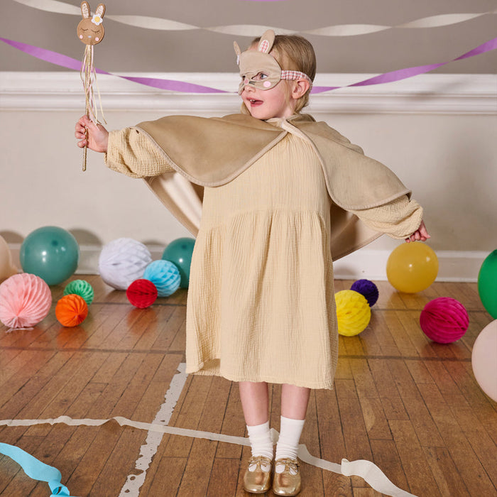 Child in a costume with a wooden rabbit figure, surrounded by colorful balloons and decorations on a wooden floor.