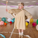 Child in a costume with a wooden rabbit figure, surrounded by colorful balloons and decorations on a wooden floor.