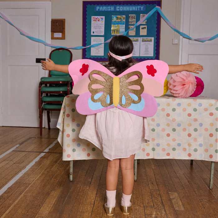 Child wearing butterfly wings in a room with a bulletin board and colorful decorations.