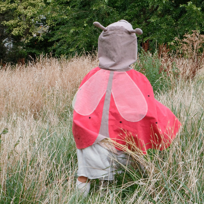 Child wearing a ladybug costume standing in a grassy field with trees in the background