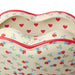 Close-up of a heart-shaped bag with a cream background, red and blue floral print, and red trim, shown open against a white background.