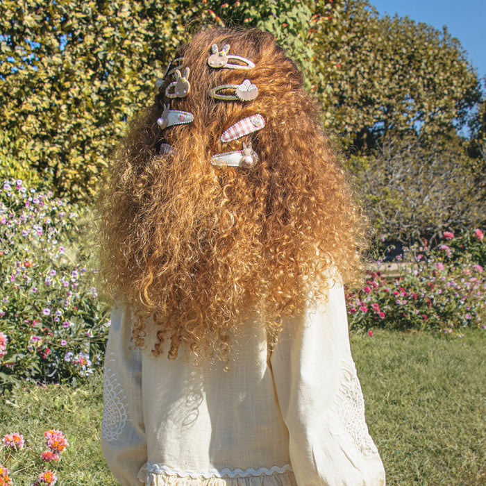Person with long, curly hair adorned with decorative hair clips in a garden setting.