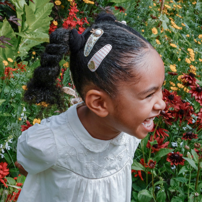 Child in a white dress standing among flowers with a joyful expression