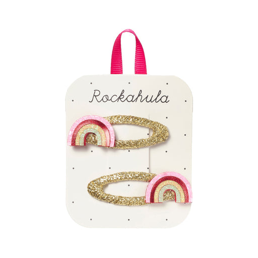 Two rainbow-shaped hair clips with gold glitter on a Rockahula branded card.