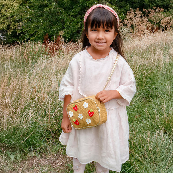 Young girl in a white dress holding a small handbag with floral designs in a grassy field.