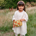 Young girl in a white dress holding a small handbag with floral designs in a grassy field.