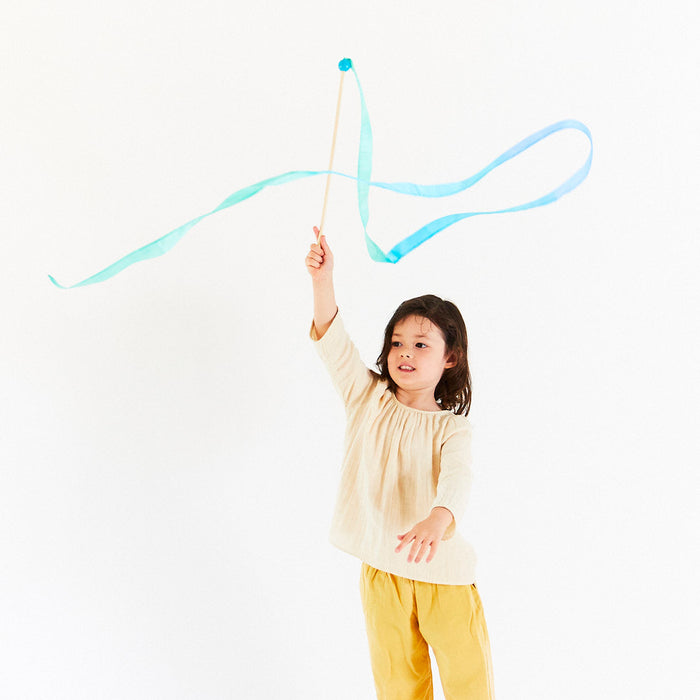 Child holding a blue ribbon on a wooden streamer wand against a white background
