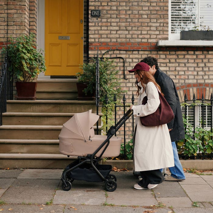 Woman pushing a stroller with a man walking behind, in front of a brick building with a yellow door.