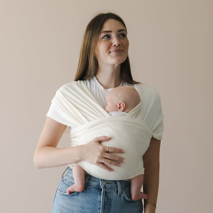 Woman holding a baby in a white sling against a plain background