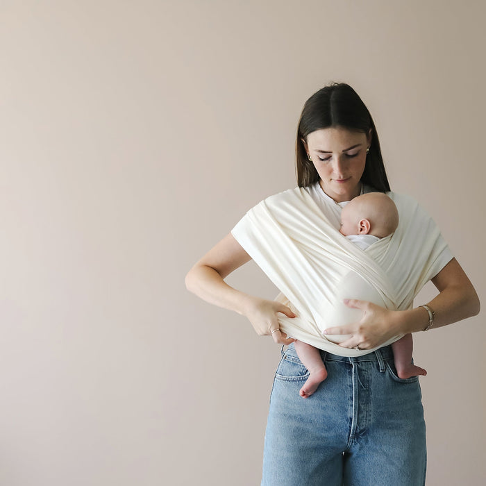 Woman holding a baby in a white wrap against a beige background