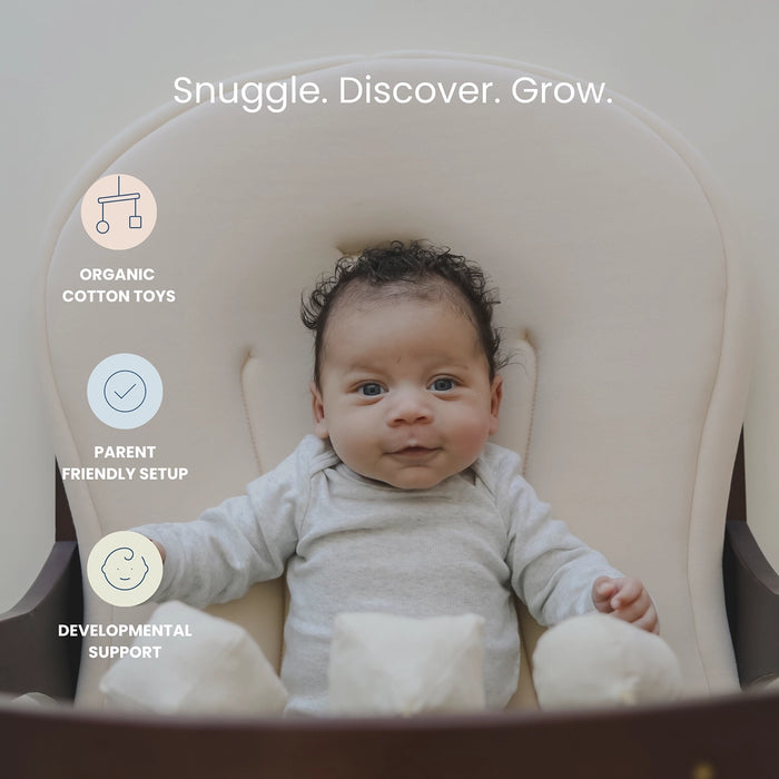 Baby in a snuggle me lounger mat with text 'Snuggle. Discover. Grow.' featuring organic cotton toys, parent friendly set up and developmental support