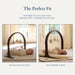 A baby activity gym with an arch-shaped dark wood frame and three hanging fabric toys, shown in two inset photos on a light beige background. Text at the top reads 'The Perfect Fit' and explains how it fits over a Snuggle Me lounger or play mat.