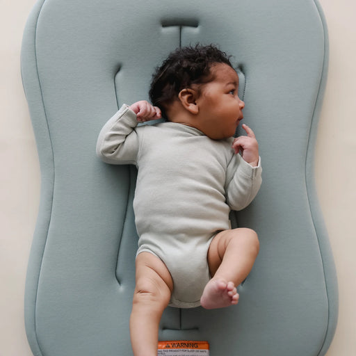 Baby lying on a slate blue infant lounger with a neutral background