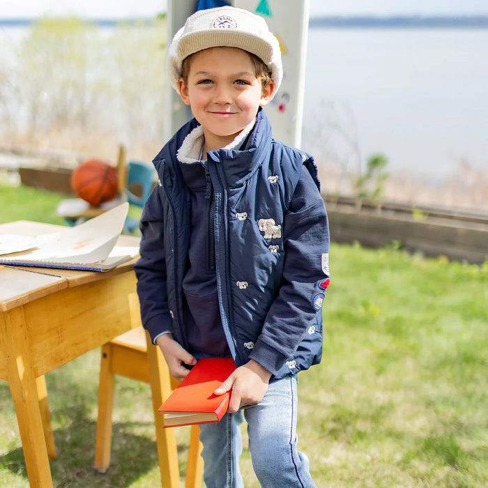 Child wearing a cream hat with navy jacket holding an orange book