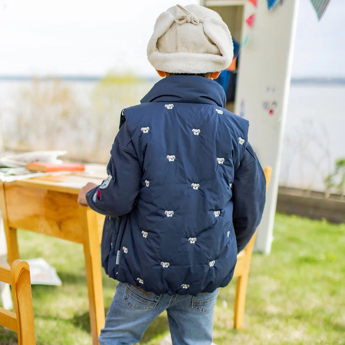 Child wearing a cream hat with navy jacket outdoors.