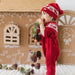 Child in red Christmas outfit standing next to a gingerbread house-themed backdrop