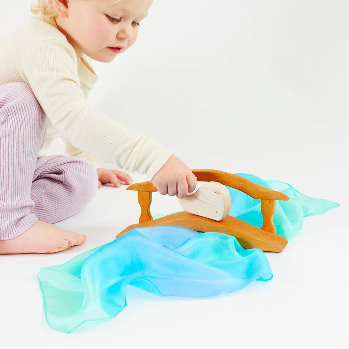 Child playing with a wooden toy atop a ocean themed Playsilk on a white surface