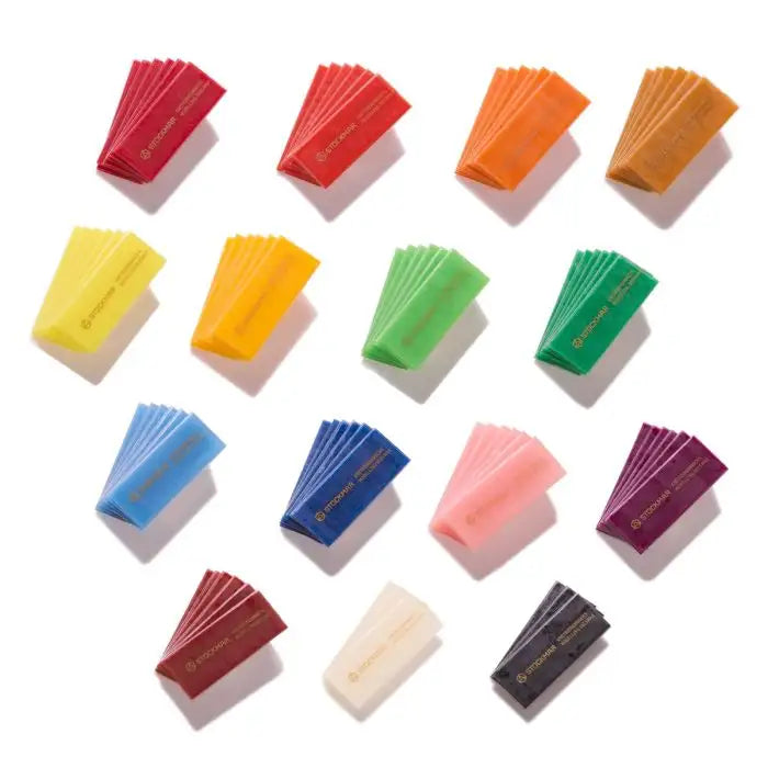 Small fanned out pieces of Stockmar modelling beeswax in multiple colors including red, orange, yellow, green, blue, pink, purple, cream, and black. Each packet has gold text that reads Stockmar.