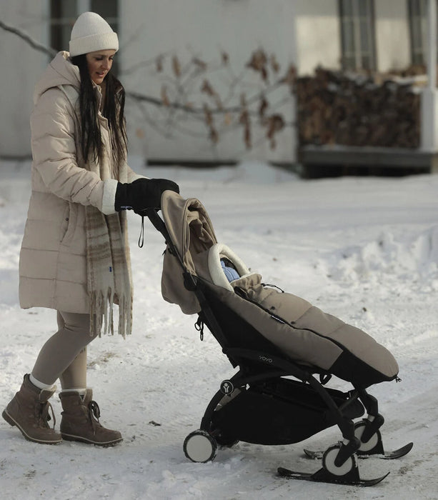 Woman in winter clothing pushing a stroller with snowshoes on a snowy path.
