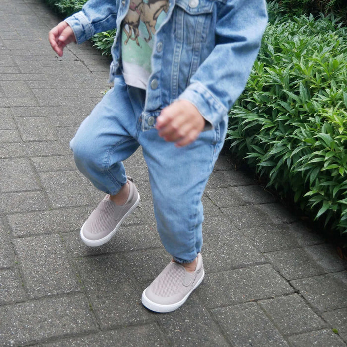 Child wearing a denim outfit with gray shoes on a paved walkway.