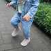 Child wearing a denim outfit with gray shoes on a paved walkway.