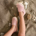 Pink slip-on shoes worn on a sandy surface with small rocks.