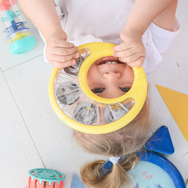 Child playing with a toy that covers their face, with colorful toys scattered around.