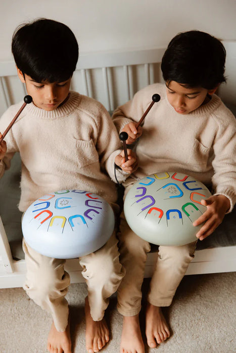 Two children playing with colorful drums indoors.