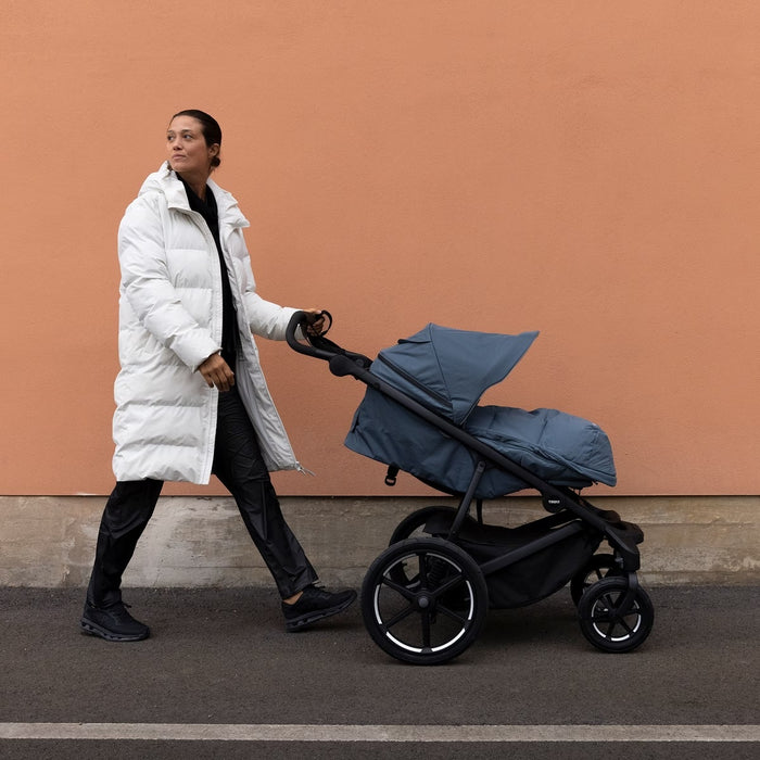 Person pushing a blue stroller against a beige wall