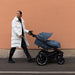 Person pushing a blue stroller against a beige wall